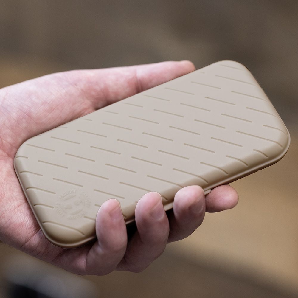 Pouzdro na šipky Harrows Slimcase Eine Hand hält ein schlankes, steingraues Etui mit einem dezenten Muster. Das Etui wirkt stabil und ist wahrscheinlich für Dartzubehör gedacht.