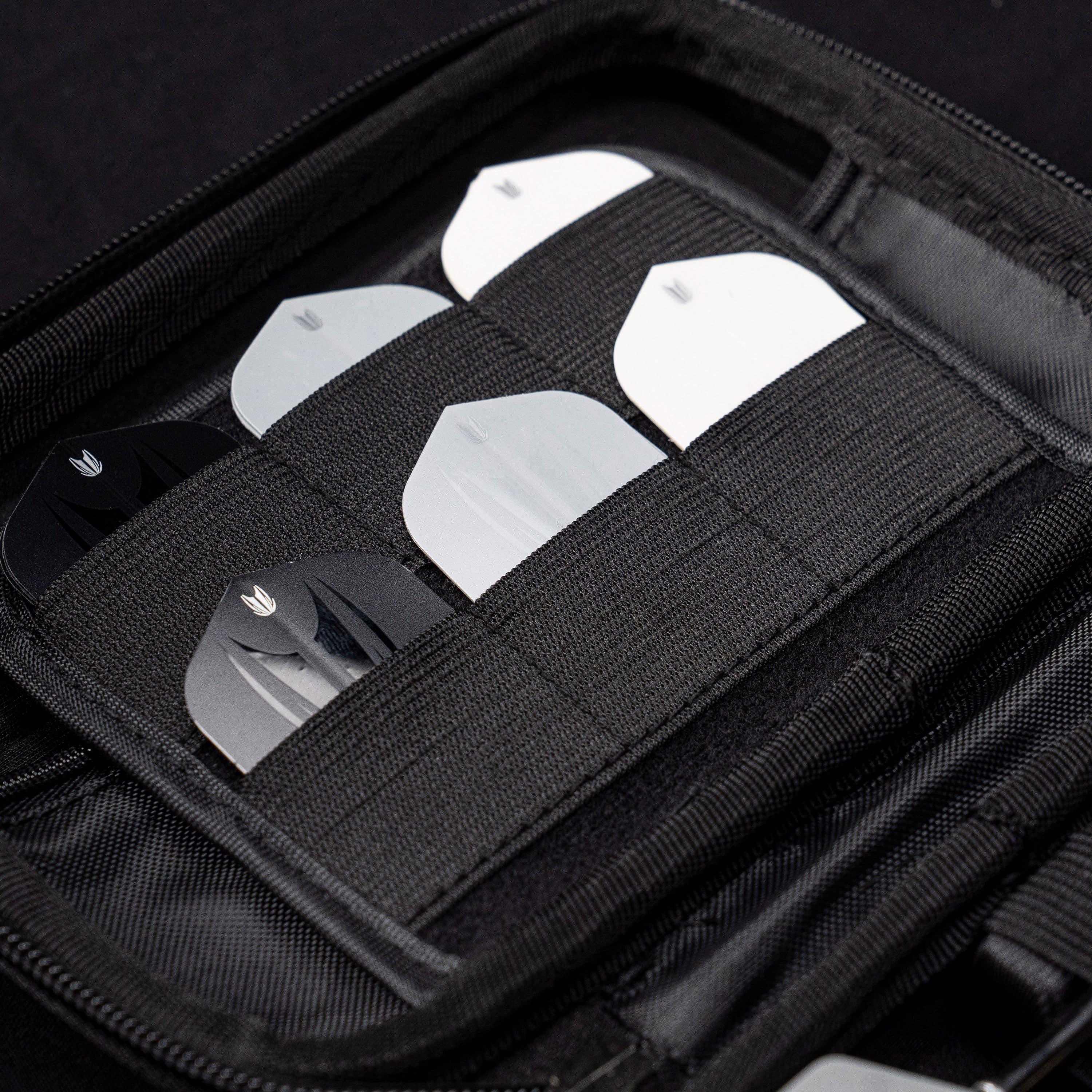 Pouzdro na šipky Target Takoma Luke Littler XL Das Bild zeigt das „Target Takoma Bolide XL Dartcase“, das mehrere Dart-Flights in schwarzen und weißen Farben organisiert aufbewahrt. Die Flights sind sicher in elastischen Halterungen im Inneren des schwarzen Etuis verstaut.