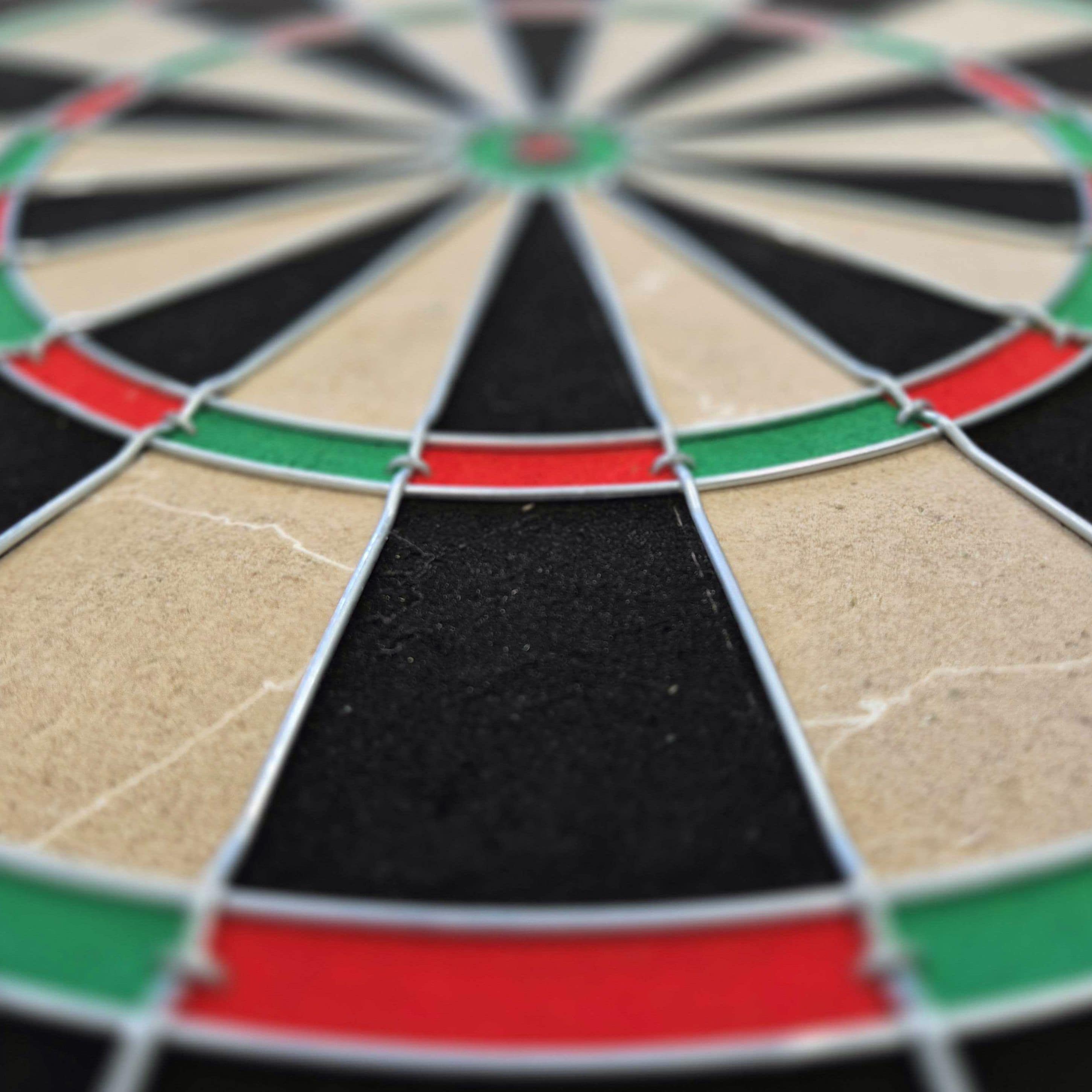 Sada ocelových terčů na terč Dimitri Van Den Bergh Das Bild zeigt eine Nahaufnahme eines Steeldartboards mit schwarz, beige, rot und grün markierten Segmenten. Besonders gut zu erkennen sind die Drähte, die die Felder voneinander trennen.