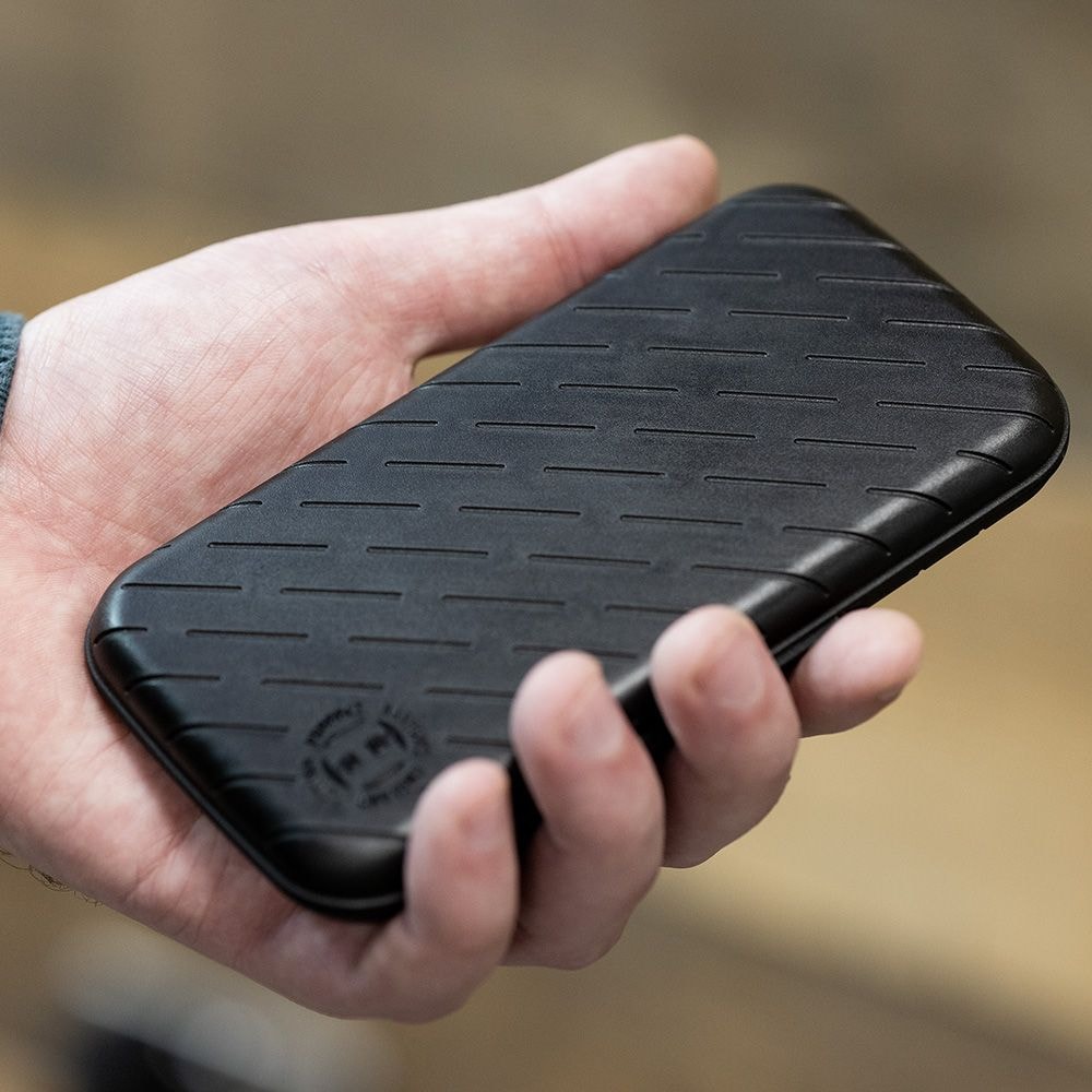 Pouzdro na šipky Harrows Slimcase Eine Person hält eine schwarze, schlanke Darttasche in der Hand. Die Oberfläche der Tasche hat ein dezentes, gerilltes Muster.
