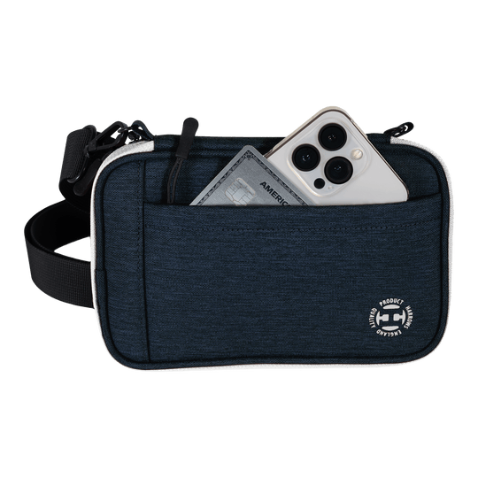 Peněženka na šipky Harrows Smart Case XL Eine blaue Tasche mit Vorderfach enthält ein Smartphone und eine Kreditkarte. Am unteren Rand der Tasche befindet sich ein rundes weißes Logo.