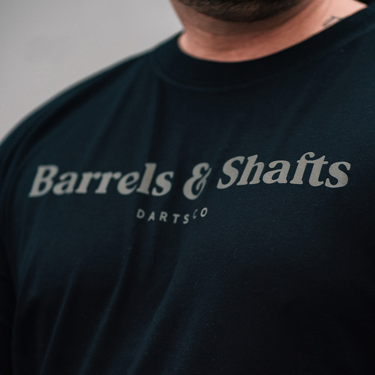 Tričko Barrels and Shafts - Černé Das Bild zeigt ein schwarzes T-Shirt mit der Aufschrift "Barrels & Shafts". Darunter steht in kleineren Buchstaben "DARTSCO".