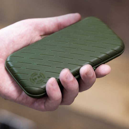 Pouzdro na šipky Harrows Slimcase Eine Hand hält ein schlankes, grünes Etui. Das Etui hat ein strukturiertes Muster und ein rundes Logo in der Ecke.