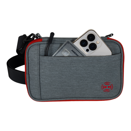 Peněženka na šipky Harrows Smart Case XL Das Bild zeigt eine graue Tasche mit rotem Rand und einem schwarzen Gurt. In der Vordertasche stecken ein Smartphone und eine Kreditkarte.