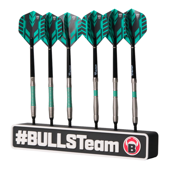 Das Bild zeigt sechs schwarze Dartpfeile mit grünen Akzenten, die ordentlich in einer Halterung stehen. Auf der Halterung steht groß "#BULLSTeam" und das Bulls-Logo ist sichtbar.