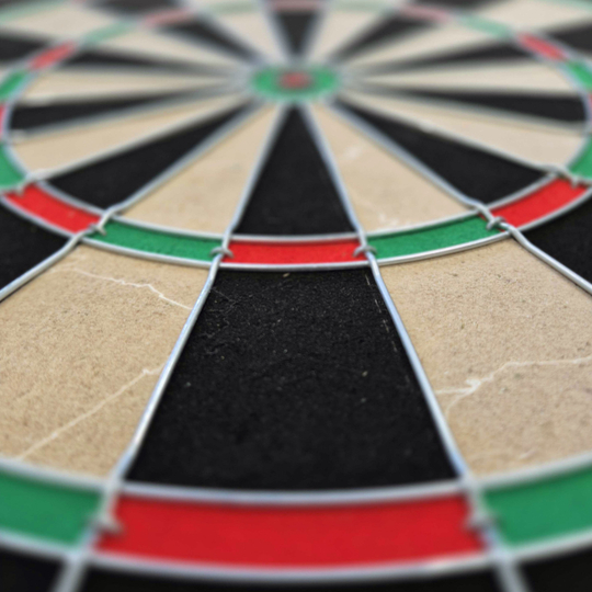 Das Bild zeigt eine Nahaufnahme eines Steeldartboards mit schwarz, beige, rot und grün markierten Segmenten. Besonders gut zu erkennen sind die Drähte, die die Felder voneinander trennen.